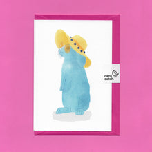 Load image into Gallery viewer, A stylised watercolour illustration of a blue rabbit wearing sunglasses and a yellow floppy sunhat on a greeting card, with a bright pink envelope held together by an eco friendly plastic free card catch sticker, on a pink background.
