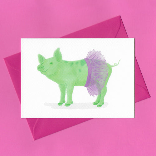 A stylised watercolour illustration of a green pig wearing a purple tutu on a greeting card, with a bright pink envelope, on a pink background