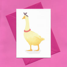 Load image into Gallery viewer, A stylised watercolour illustration of a yellow goose, wearing a purple headscarf and red beaded necklace, on a greeting card, with a bright pink envelope, on a pink background
