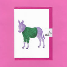 Load image into Gallery viewer, A stylised watercolour illustration on a greeting card of a purple donkey wearing a green zigzag patterned jumper, with a bright pink envelope held together by an eco friendly plastic free card catch sticker, on a pink background
