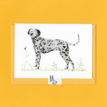 Load image into Gallery viewer, A stylised watercolour illustration on a luxury greeting card of a black and white Dalmatian dog amongst grass and wildflowers and a bee, with a bright yellow envelope held together with an eco friendly plastic free card catch sticker, on a yellow background
