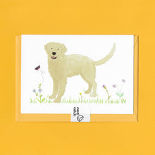 Load image into Gallery viewer, A stylised watercolour illustration on a luxury greeting card of a golden retriever dog amongst grass and wildflowers and a butterfly, with a bright yellow envelope held together with an eco friendly plastic free card catch sticker, on a yellow background
