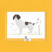 Load image into Gallery viewer, A stylised watercolour illustration on a luxury greeting card of a brown and white spaniel dog amongst grass and wildflowers and a bee and butterfly, with a bright yellow envelope held together with an eco friendly plastic free card catch sticker, on a yellow background
