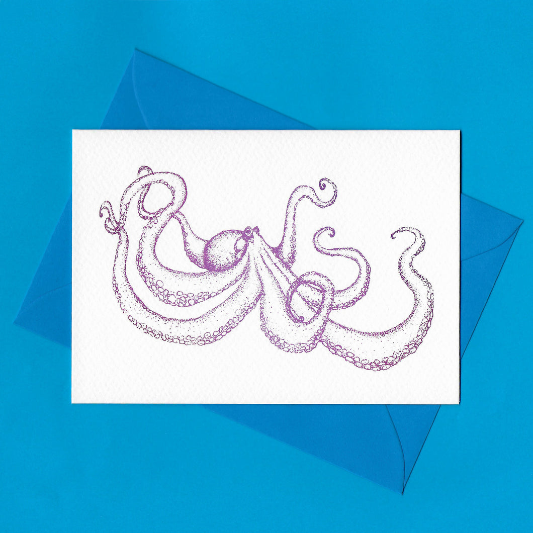 A detailed colour illustration on a luxury greeting card of a purple coloured octopus, with a kingfisher blue envelope, sitting on a blue background