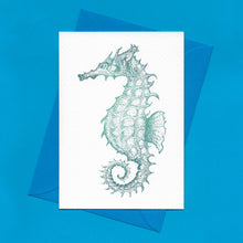 Load image into Gallery viewer, A detailed colour illustration on a luxury greeting card of a teal coloured seahorse, with a kingfisher blue envelope, sitting on a blue background
